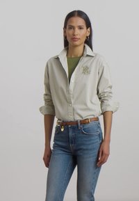 Csíkos gombos ing világos zöld és fehér színben, amelyen egy logó található a mellkason. Zöld felsőre és kék farmerral, valamint barna övvel viselik.