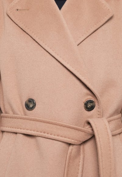 Beige topelt lõpuni kinnitatud mantel pehmest kangast, millel on kohandatud krae, mustad nupud ja sobiv vöö, mis on seotud talje ümber.