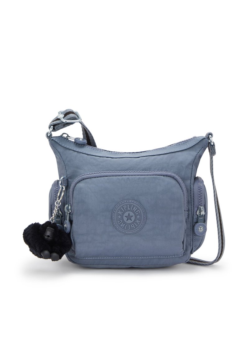 Borsa a spalla in tessuto blu testurizzato con una tasca frontale con zip, un patch rotondo con logo e un portachiavi a forma di scimmia pelosa attaccato.