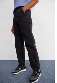 Zwarte denim broek met een rechte pasvorm, voorzien van voorzakken en subtiele stiksels, gecombineerd met zwart-grijze sport sneakers.