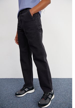 Black denim trousers with a straight cut, featuring front pockets and subtle stitching details, paired with black and gray athletic sneakers.