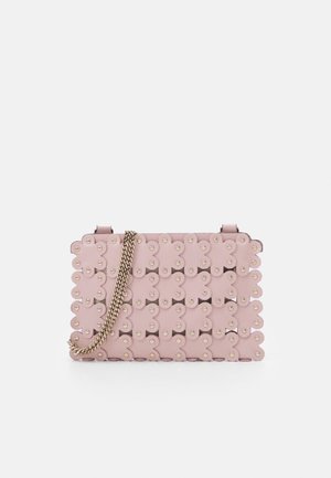 Sac à main rose clair avec un motif floral ajouré et des clous dorés, doté d’une bandoulière chaîne dorée sur fond blanc.