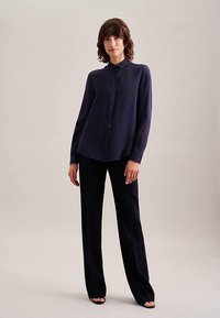 Camicia blu navy a maniche lunghe con bottoni e colletto, abbinata a pantaloni su misura dello stesso colore; entrambi con una texture liscia e un design aderente.