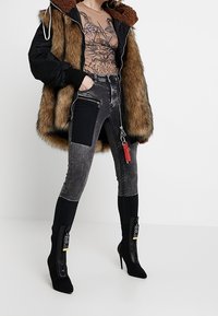 Černá bunda podšitá kožešinou, vzorované béžové tričko, šedé jeansy s vysokým pasem a záplatami, a černé boty na podpatku se zipy a štítky.