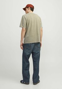 Grå bomulds T-shirt med korte ærmer, parret med løstsiddende denim jeans. Personen bærer en rød kasket og sorte sneakers.