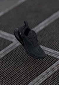 Svart sneaker med ett texturerat meshdäck, snörning och vadderad tunga. Har en framträdande svart luftkuddsenhet i sulan.