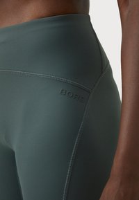 Magas derekú leggings sötétzöld anyagból. Tűzött varrásokkal és gumi „BORG” logóval a derékrész oldalán.