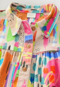 Chemise à col colorée avec un mélange de motifs, mettant en avant des teintes vives comme le rose, l'orange et le vert, avec des détails de boutons en bois.