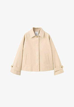 Veste courte beige à manches larges, avec un seul bouton visible au col, deux poches fendues sur le devant et des poignets boutonnés.