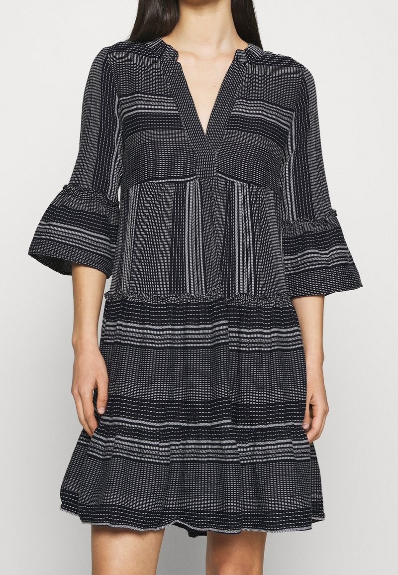 Femme portant une robe à motifs noir et blanc avec des manches trois-quarts évasées et un col en V.