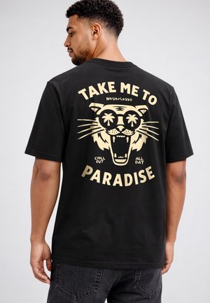 Mann trägt ein schwarzes T-Shirt mit einer Grafik eines brüllenden Tigers mit Sonnenbrille, Palmen und Text "Take me to paradise, chill out all day."
