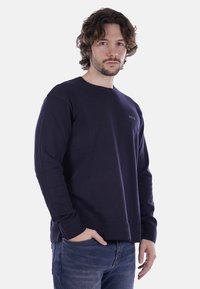 Felpa girocollo della marina in misto cotone, con dettagli a costine sulle spalle e sui polsini, abbinata a jeans in denim blu.