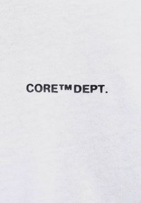Valkoinen puuvillakangas, jossa on tekstuuripinta, ja jonka keskellä on painettuna rohkeasti mustilla kirjaimilla "CORE™ DEPT."