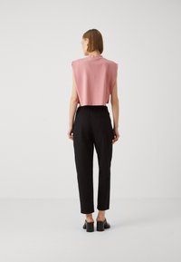 Korte roze top met aangeknipte mouwen en hoge halslijn, gecombineerd met zwarte tapered broek en zwarte chunky-gehakte schoenen.