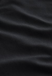 Tissu noir lisse avec de doux plis et une légère brillance, montrant la texture et des reflets de lumière doux.