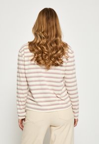 Langærmet top i creme med tynde vandrette pink striber. Blødt materiale, afrundet kant og subtile manchet-detaljer. Sæt med lyse beige bukser.