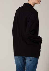 Camicia overshirt nera in cotone con colletto, maniche lunghe e vestibilità rilassata; presenta tasche laterali e orlo dritto.