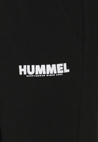 HUMMEL-logo met de tekst "SPORTKLEDING SINDS 1923" in het wit gedrukt op zwart textiel, waarschijnlijk een kledingstuk.