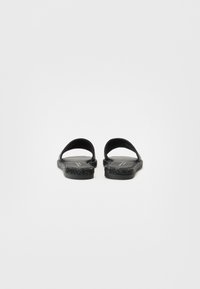 Sorte sandaler med to brede stropper, teksturert overflate, flat såle og subtil glitrende detalj på kantene. Bakfra, minimalistisk design.
