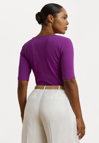 Top ribbed viola con maniche corte, abbinato a pantaloni bianchi a gamba larga e una cintura intrecciata color beige, che mette in mostra una texture liscia e un design aderente.