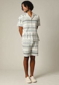 Korte mouwen, overhemd met kraag en bijpassende korte broek in zwart-wit geometrisch patroon. Lichtgewicht stof met een ontspannen pasvorm. Beige instapschoenen.