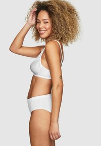 Vit bh och matchande boyshorts i mjukt material, med tunna axelband och en delikat spetskant på bh:n. Lockigt hår synligt.
