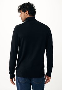 Zwarte trui met een hoge kraag, geribde manchetten en een ontspannen pasvorm, gecombineerd met blauwe jeans. Gladde textuur en minimalistisch design.