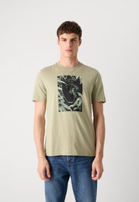 Olivengrønn kortermet t-skjorte med et svart og grønt grafisk bilde av et leopardansikt, kontrasterende kjededesign under bildet.