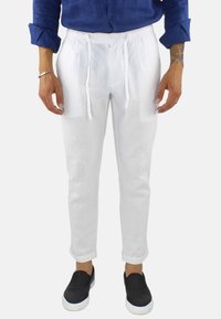 Pantaloni bianchi in lino con vita elastica e cordoncino, dotati di tasche laterali e una silhouette a gamba affusolata, indossati con scarpe nere senza lacci.