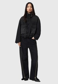 Veste en denim noir avec un col haut, des poches avant et un design court. Associée à un jean noir à jambes larges avec des zips sur les côtés.