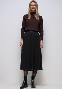 Musta nilkkapituisen hameen kerroksellinen malli ja joustava vyötärönauha, yhdistetty ruskeaan poolopaitaan ja mustiin nilkkureihin. Sileäpintainen materiaali.