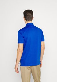 Royalblå polo med slät tyg, med krage, korta ärmar och sidoklyftor i fållen för ökad komfort.