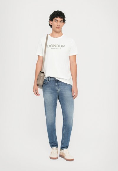 White cotton t-shirt with "DON DUP MADE IN ITALY" text, paired with light blue jeans and beige sneakers, holding a small gray crossbody bag.