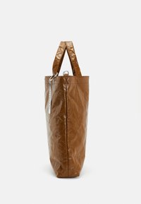 Sac fourre-tout en papier brun avec une surface texturée, deux courtes poignées et un accent en métal argenté. Forme cylindrique avec un fond plat.
