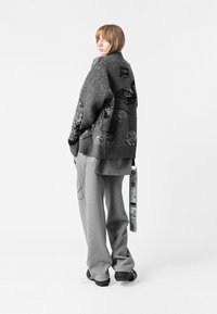 Suéter gris de punto extragrande con patrones abstractos negros, combinado con pantalones grises sueltos. Incluye una etiqueta y un detalle de correa.