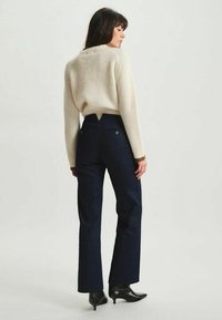 Pull en maille côtelée crème et pantalon en denim foncé taille haute. Le pantalon a des poches latérales et est assorti à des bottes à talons noirs élégantes.