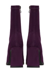 Botines de ante morados con una textura suave, tacones cuadrados y cierre de cremallera, con detalles de costura en contraste.
