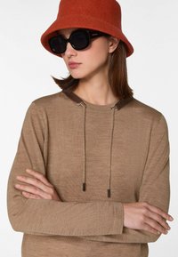 Pull en tricot marron avec un col rond, featuring un empiècement texturé et des cordons de serrage. Porté avec un chapeau seau en feutre orange et des lunettes de soleil noires.