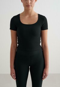 Top negro de manga corta con textura acanalada y escote redondeado. La tela es suave y ajustada, combinada con leggings acanalados de tiro alto a juego.
