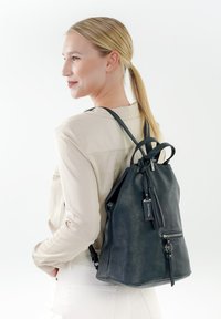 Zaino in pelle nera con chiusura a coulisse, zip prominente e dettagli con fiocco. Texture morbida con spallacci regolabili.