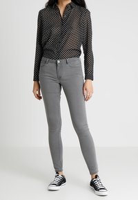 Black polka dot button-up shirt, long sleeves; fitted gray jeans, ankle-length; black and white sneakers. Smooth fabric, classic design.