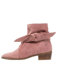 Botte de cheville en suede rose avec un détail de nœud noué, un bout pointu et un talon en bois empilé. Présente des accents de couture et un logo sur le côté.