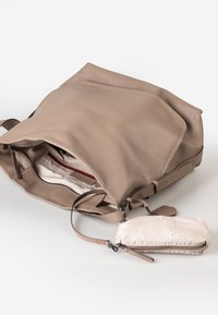 Beige leren handtas met open rits die de lichte stoffen interieur toont, eraan bevestigd een kleine gestreepte beige pouch met rits op een witte achtergrond.
