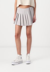 Šedá skládací sukně s vysokým pasem a rozšířeným tvarem. Spárovaná s bílými sneakers nad kotníky. Hladká textura a jednoduchý design.