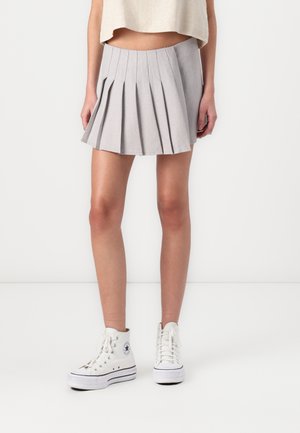 Grauer, plissierter Rock mit hoher Taille und ausgestellter Form. Kombiniert mit weißen High-Top-Sneakern. Glatte Textur und schlichtes Design.