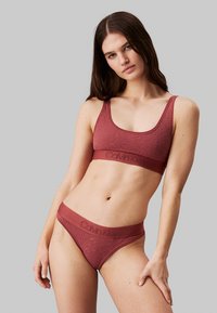 Bralette color bordeaux di Calvin Klein con un motivo testurizzato e fascia con logo, abbinato a uno string thong con un design simile. Tessuto morbido.
