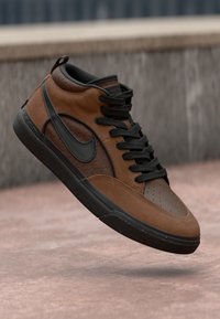 Braune High-Top-Sneaker mit schwarzer Sohle und Schnürsenkeln, schwarzem Swoosh-Logo und gemustertem Seitenpanel, schwebend über einer Betonoberfläche.