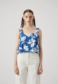 Blue floral tank top with a square neckline, featuring white flower patterns, made from lightweight fabric, paired with white pants.