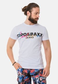 Weißes T-Shirt mit kurzen Ärmeln, das mit buntem "CIPOBAXX Exclusive Jeans"-Text bedruckt ist. Kombiniert mit blau-rot gemusterten Cargo-Shorts.