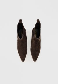 Rudos suedų kulkšninių booti su smailiu priekiu, minimalistiniu dizainu ir traukti kilpelėmis gale, kad būtų lengviau dėvėti. Lygūs padas, be matomų detalių.